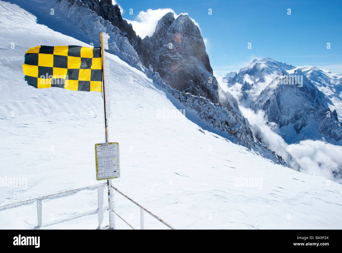 Lawinenwarnflagge (4/5, hohes Risiko) auf dem Gipfel von Grands Montets, Chamonix, Frankreich. Das Mont Blanc Massiv ist im Hintergrund zu sehen. Stockfoto