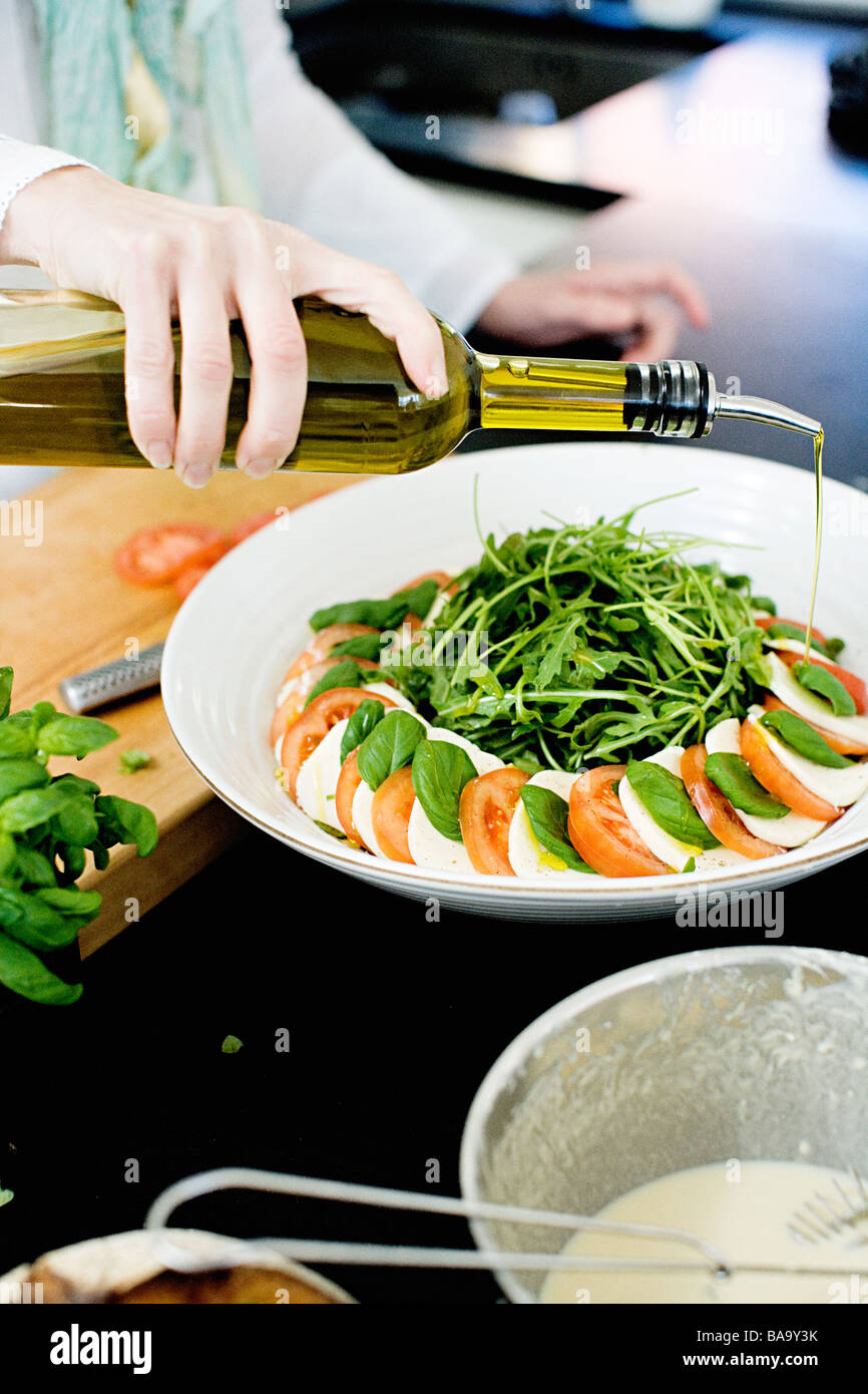 Eine Hand Gießen eine Flasche Olivenöl über Tomaten und Mozzarella. Stockfoto