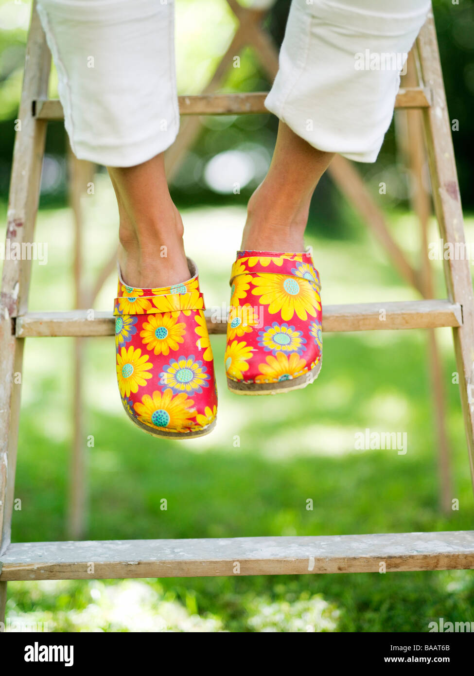 Eine Frau trägt blumige Clogs sitzen auf einer Leiter, Stockholm, Schweden. Stockfoto