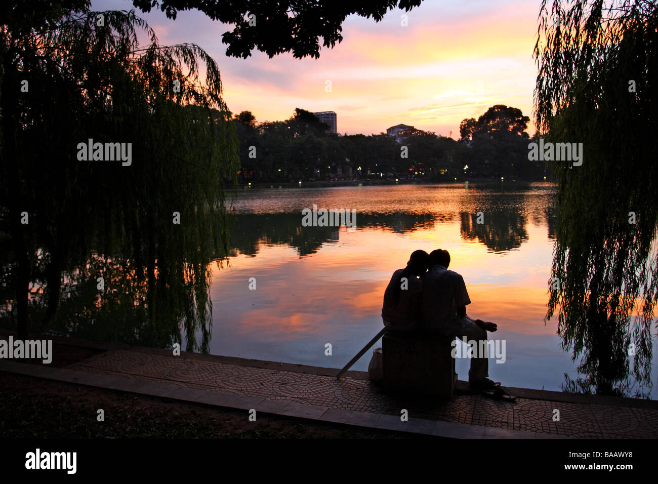 Straßenszene. Ein paar sitzt vor einem wunderschönen Sonnenuntergang am Hoan-Kiem-See. Hanoi, Vietnam Stockfoto