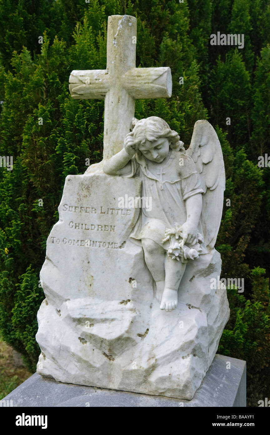Statue eines Engels neben einem Kreuz mit der Inschrift "Leiden Kleinkinder kommen auf mich" Stockfoto