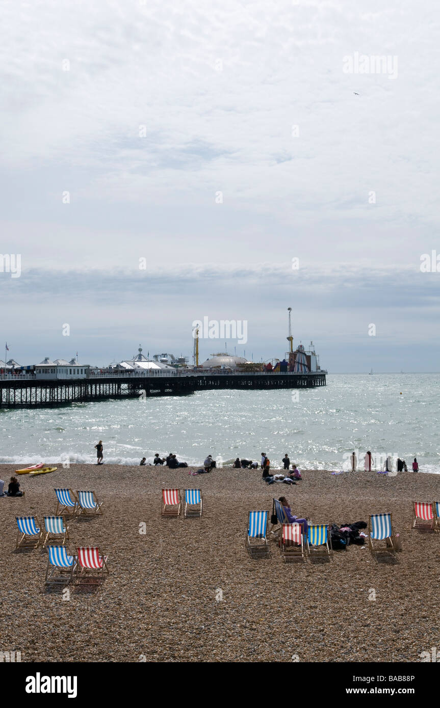 Blick über einen Kiesstrand, übersät mit Liegestühlen in Richtung Brighton Pier. Stockfoto