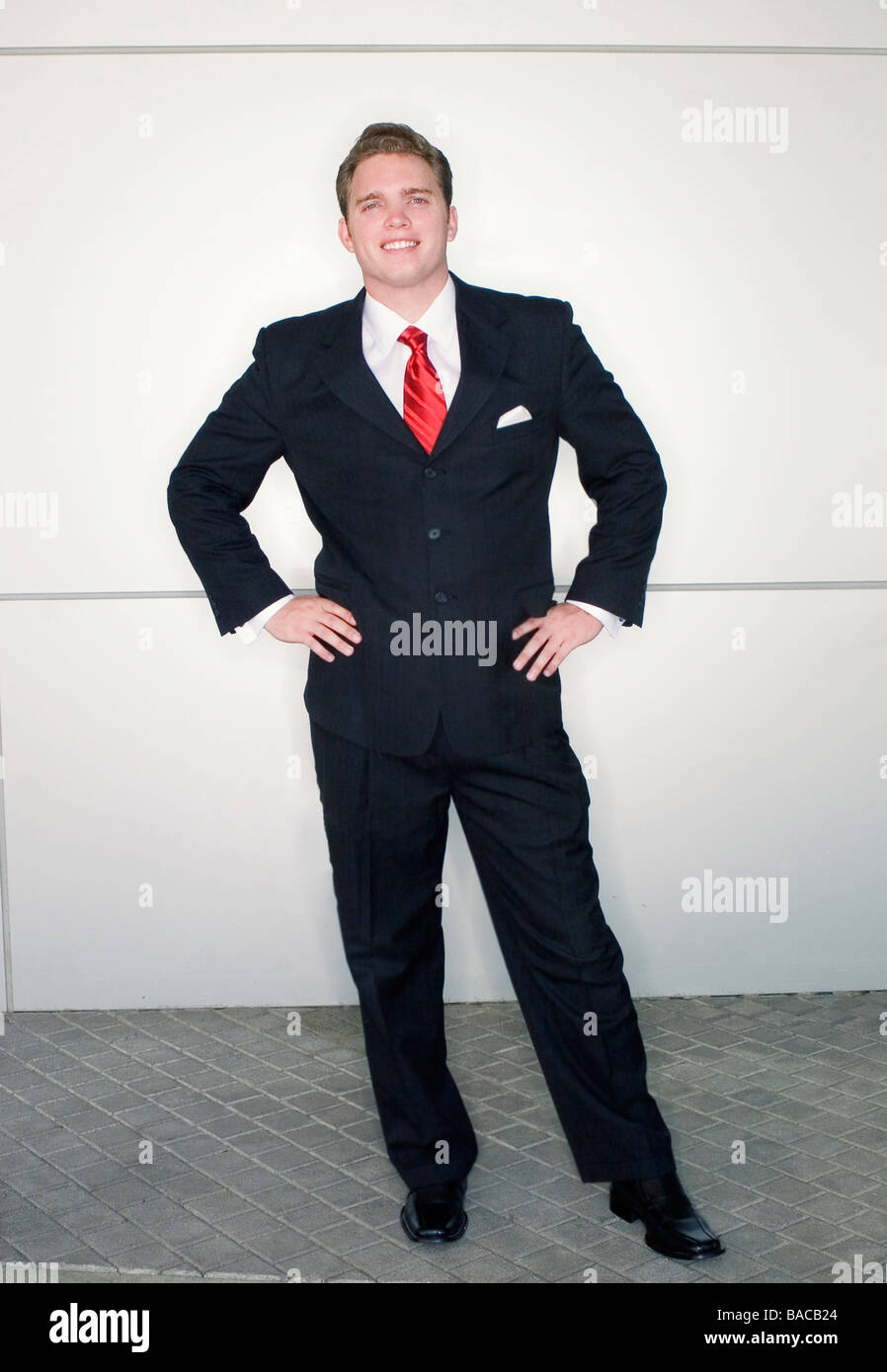 Business-Mann in rote Krawatte und schwarzen Anzug stehen in dynamischer Pose vor einem metallischen Hintergrund Stockfoto