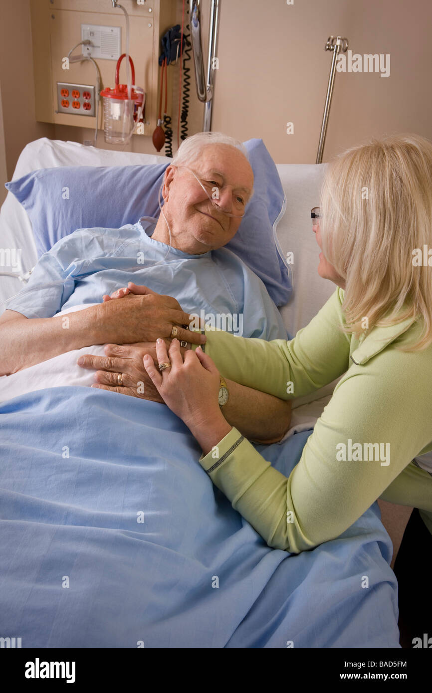 Älterer Mann und seine Tochter; Frau eines Mannes Krankenhausbett sitzen Stockfoto