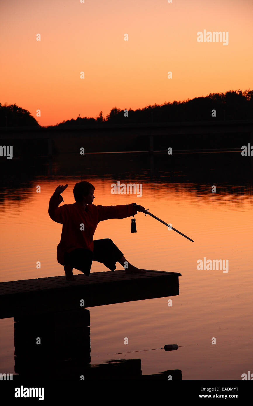 Eine junge Dame in der Silhouette auf einem Steg am Sonnenuntergang üben Tai Chi mit einem Schwert Limousin-Frankreich Stockfoto