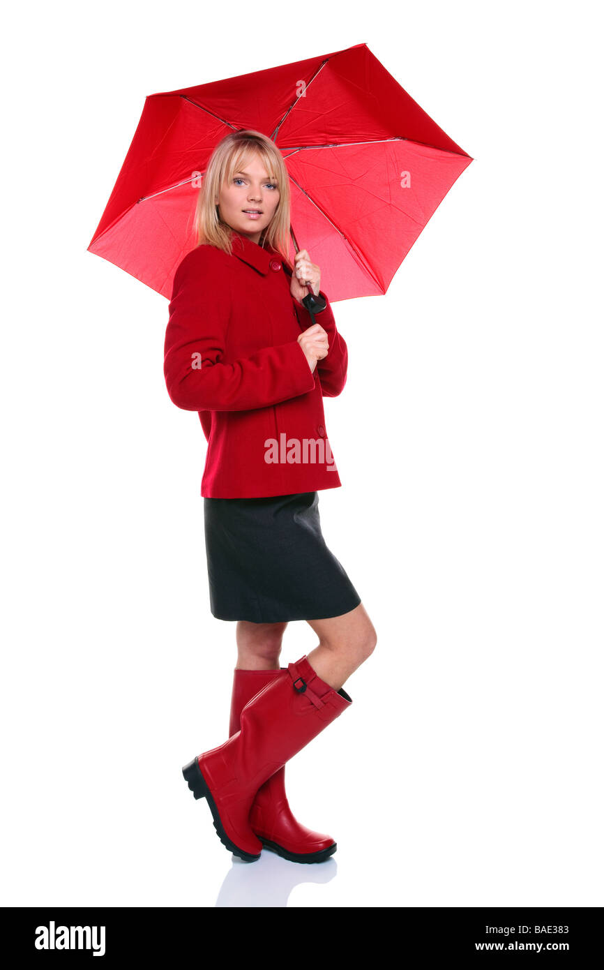 Schöne junge Frau trägt einen roten Mantel und Wellie Stiefel halten einen roten Regenschirm isoliert auf weißem Hintergrund Stockfoto