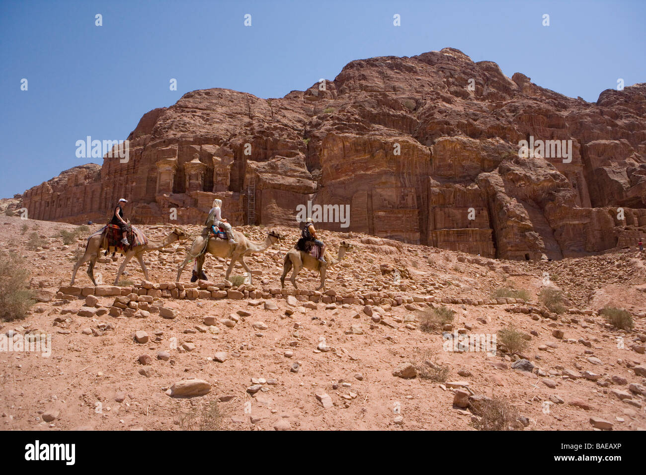 Touristen auf gemieteten Kamelen fahren vorbei an Royal Nabatäer Gräber geschnitzt in den Sandstein in der antiken Stadt Petra, Jordanien Stockfoto