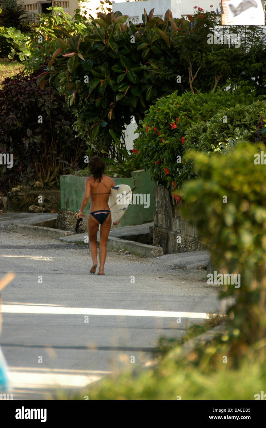 Ein Mädchen trägt einen Bikini und tragen ihr Surfbrett geht eine Straße Stockfoto