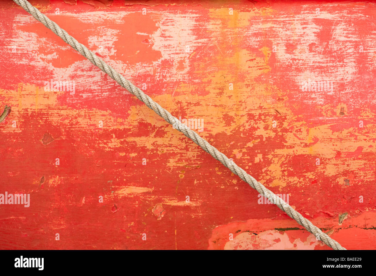 Detail der erodierten Schichten der peeling-rote Lackierung auf dem Rumpf eines Bootes im Hafen mit einem Seil diagonal überqueren Stockfoto