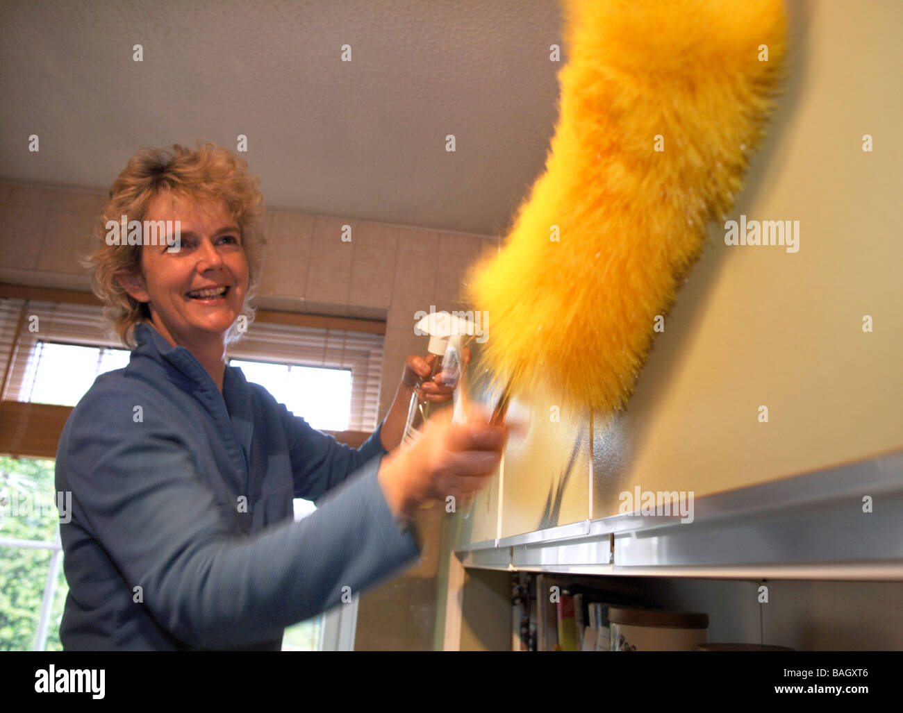 Blonde kurzhaarige Frau Reinigung Küche mit Tuch und Staubtuch auf einem stick Stockfoto