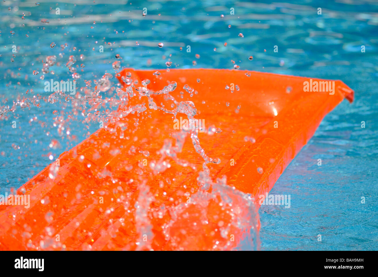 Spritzwasser über eine orange Luftmatratze schwimmend in einem Schwimmbad. Stockfoto