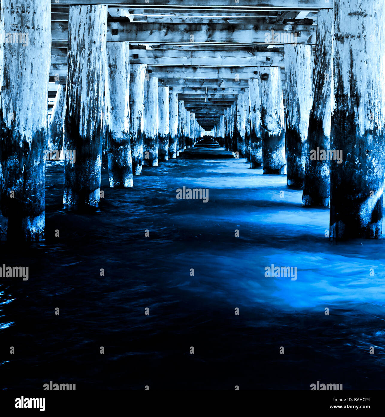 Langen, dunklen Tunnel unter dem hölzernen Pier von tief blau und kaltem Meerwasser überflutet. Nostalgische Licht und Schatten. Stockfoto