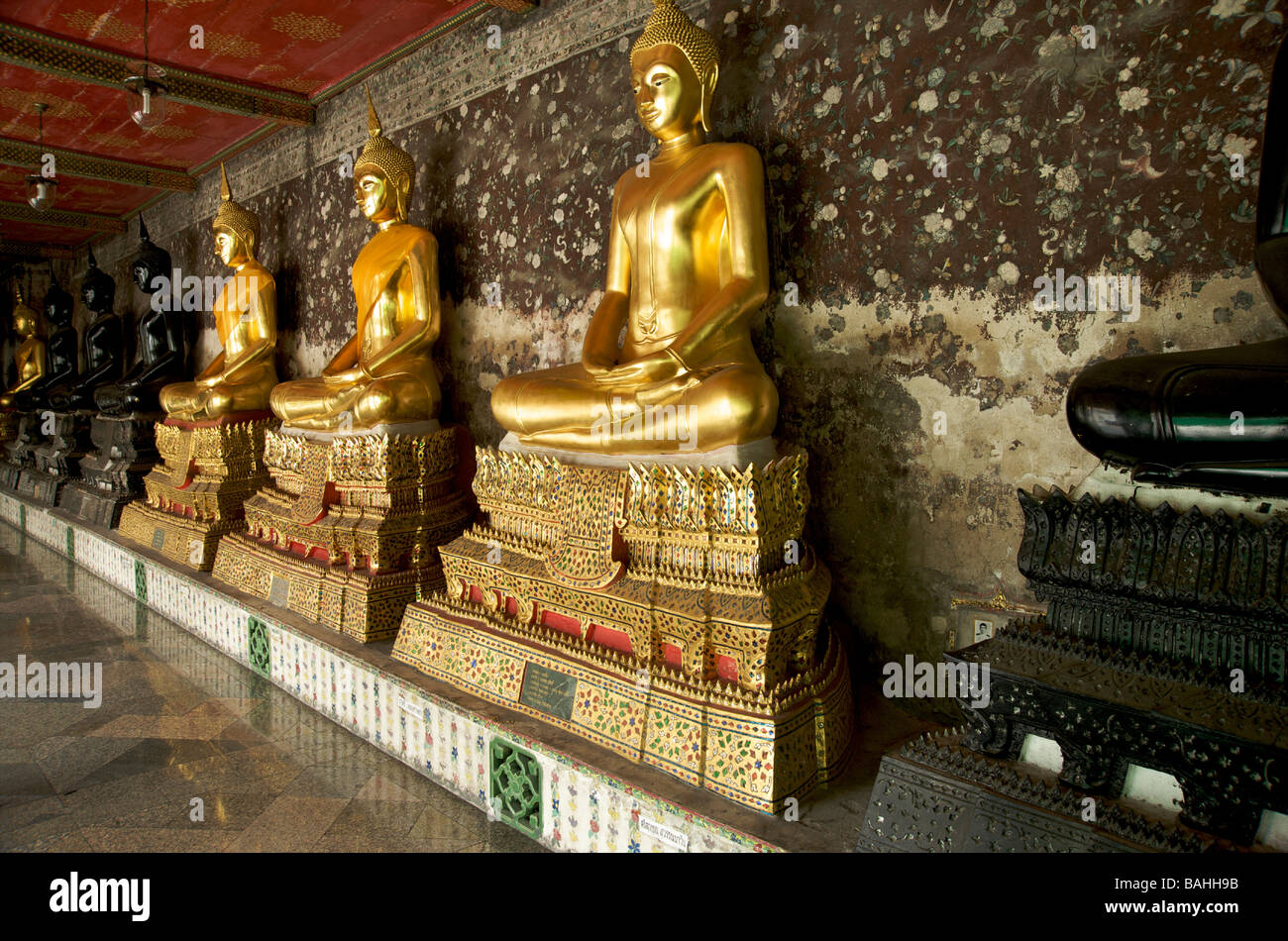 Eine Reihe von schwarzen und goldenen Buddha-Statuen säumen die Galerien im Wat Suthat Tempel in Bangkok Thailand Stockfoto