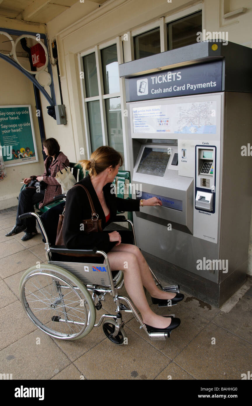 Frau in einem Rollstuhl Einkauf ein Bahn Ticket von einem Automaten am Bahnhof England UK Stockfoto