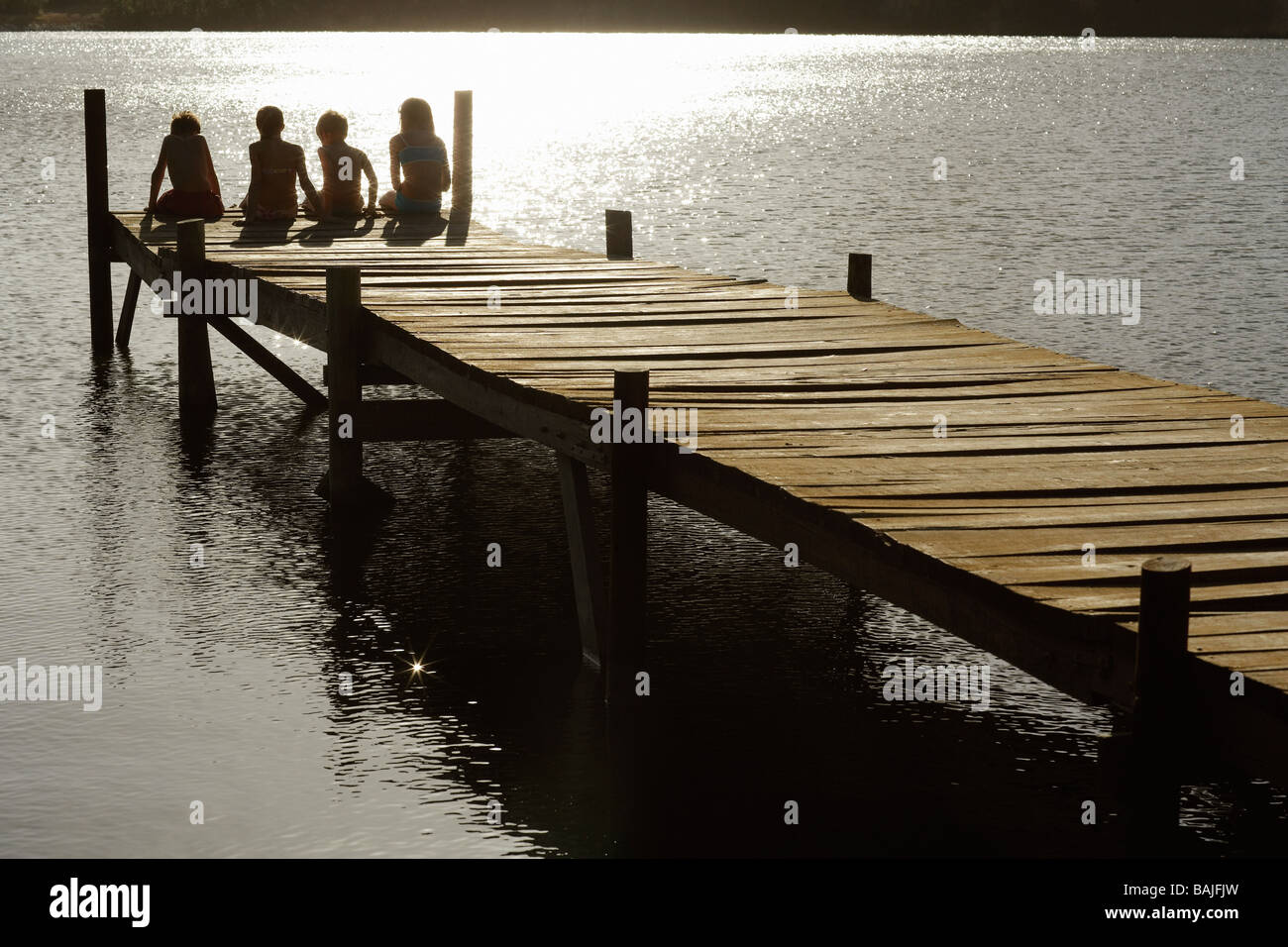Vier Kinder (7-9) sitzen auf Dock See, Ansicht von hinten. Stockfoto