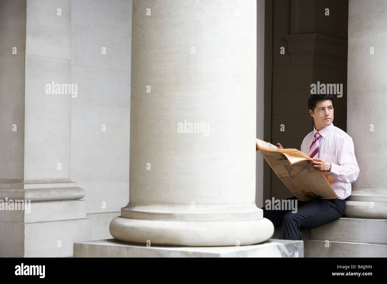 Geschäftsmann, sitzen auf Säule unter Gebälk lesen Zeitung Stockfoto