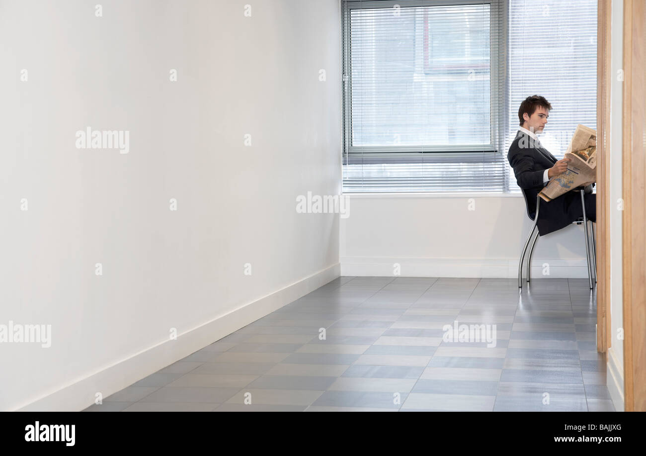 Geschäftsmann, sitzen im leeren Raum lesen Zeitung, Seitenansicht Stockfoto