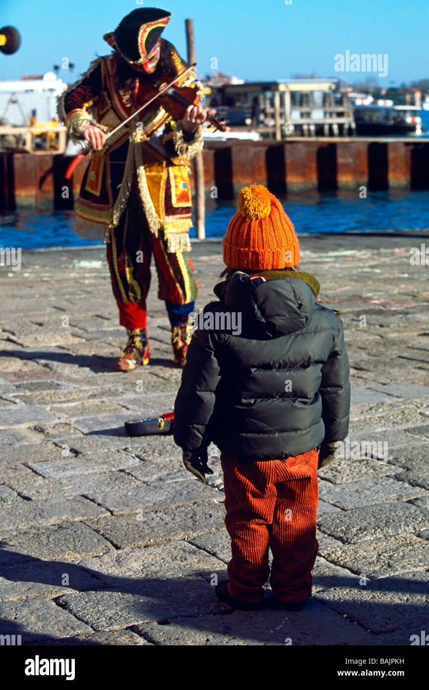 Kleiner Junge beobachten Fiddler in mittelalterlichen Kostümen auf dem Kai am Karneval in Venedig-Italien Stockfoto