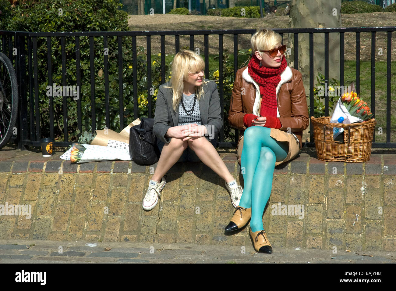 Modebewusste junge Frauen entspannen in der Sonne am Columbia Road Sonntag Blume Markert in London UK Stockfoto