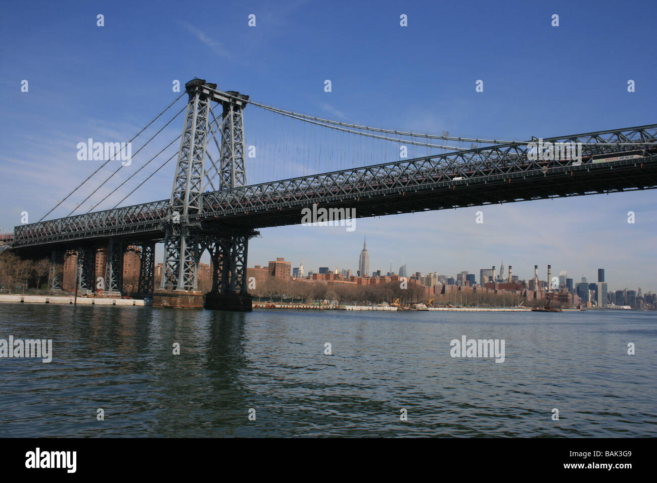 Williamsburg Bridge entlang des East River (Empire State Building im Hintergrund). Stockfoto