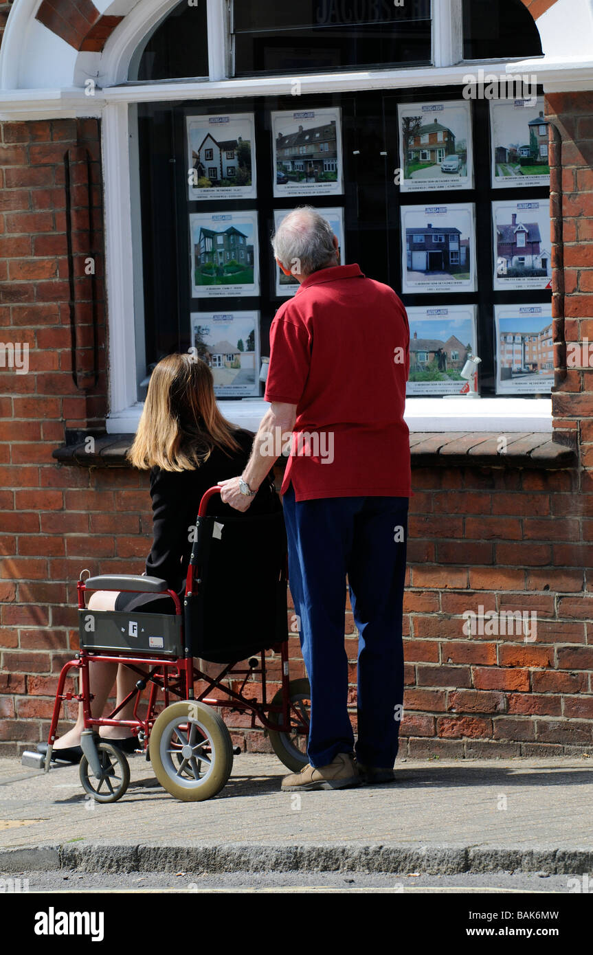 Männliche Pflegekraft schiebt Rollstuhl und weibliche Benutzer betrachten Immobilien zum Verkauf in Immobilienmakler Fenster Stockfoto