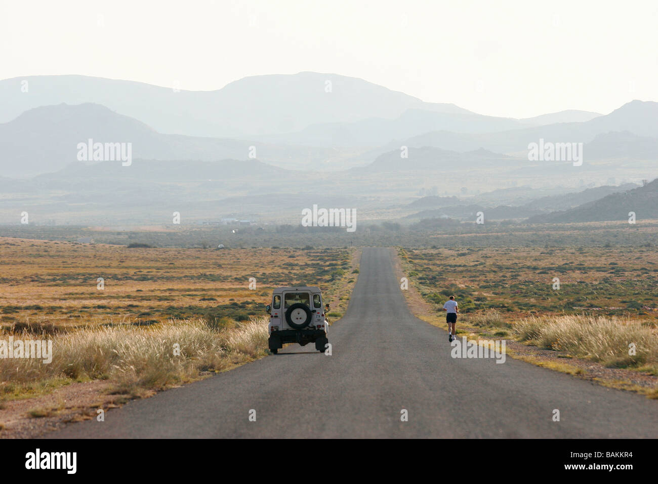 Ein Mann läuft auf einer Straße, die führt in die Ferne wie ein Fahrzeug weiter zu ihm für die Unterstützung in der Provinz Northern Cape fährt Stockfoto