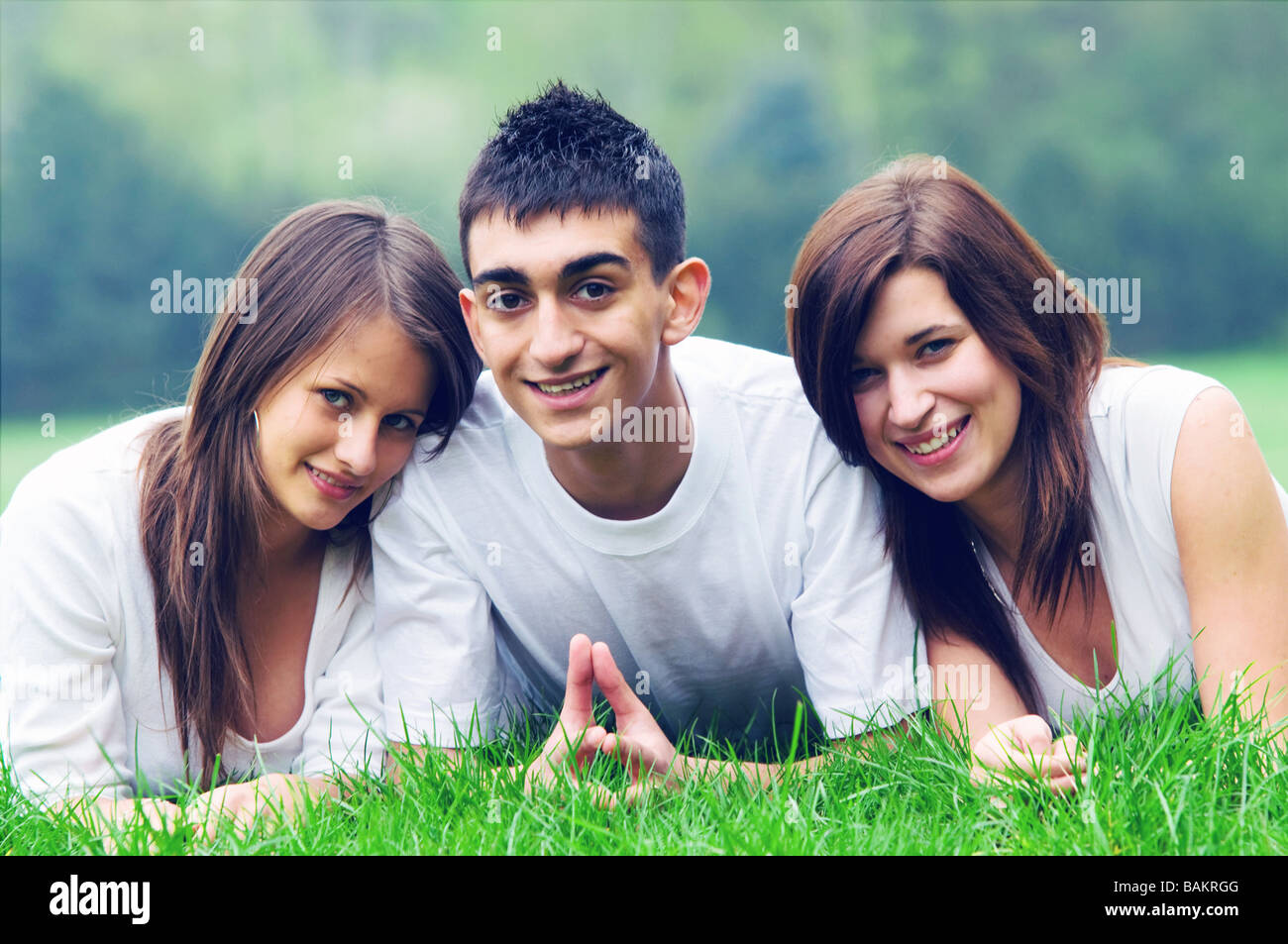 Drei junge Freunde glücklich zusammen auf dem Rasen liegen und lächelnd außerhalb Stockfoto