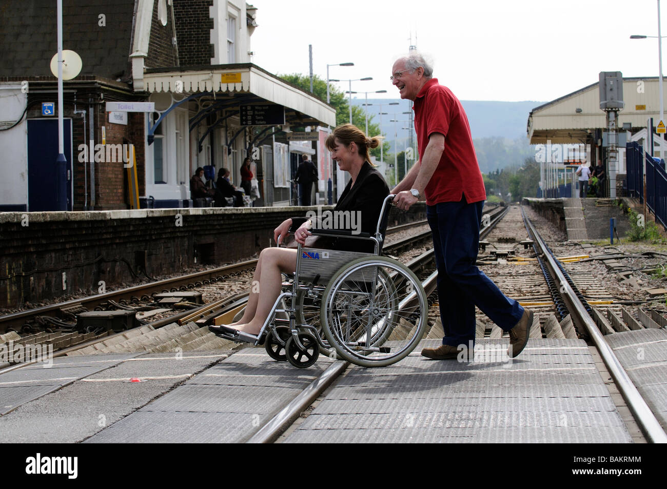 Weibliche ungültig Rollstuhlfahrer und männliche Pfleger mit einem Bahnübergang England UK Stockfoto