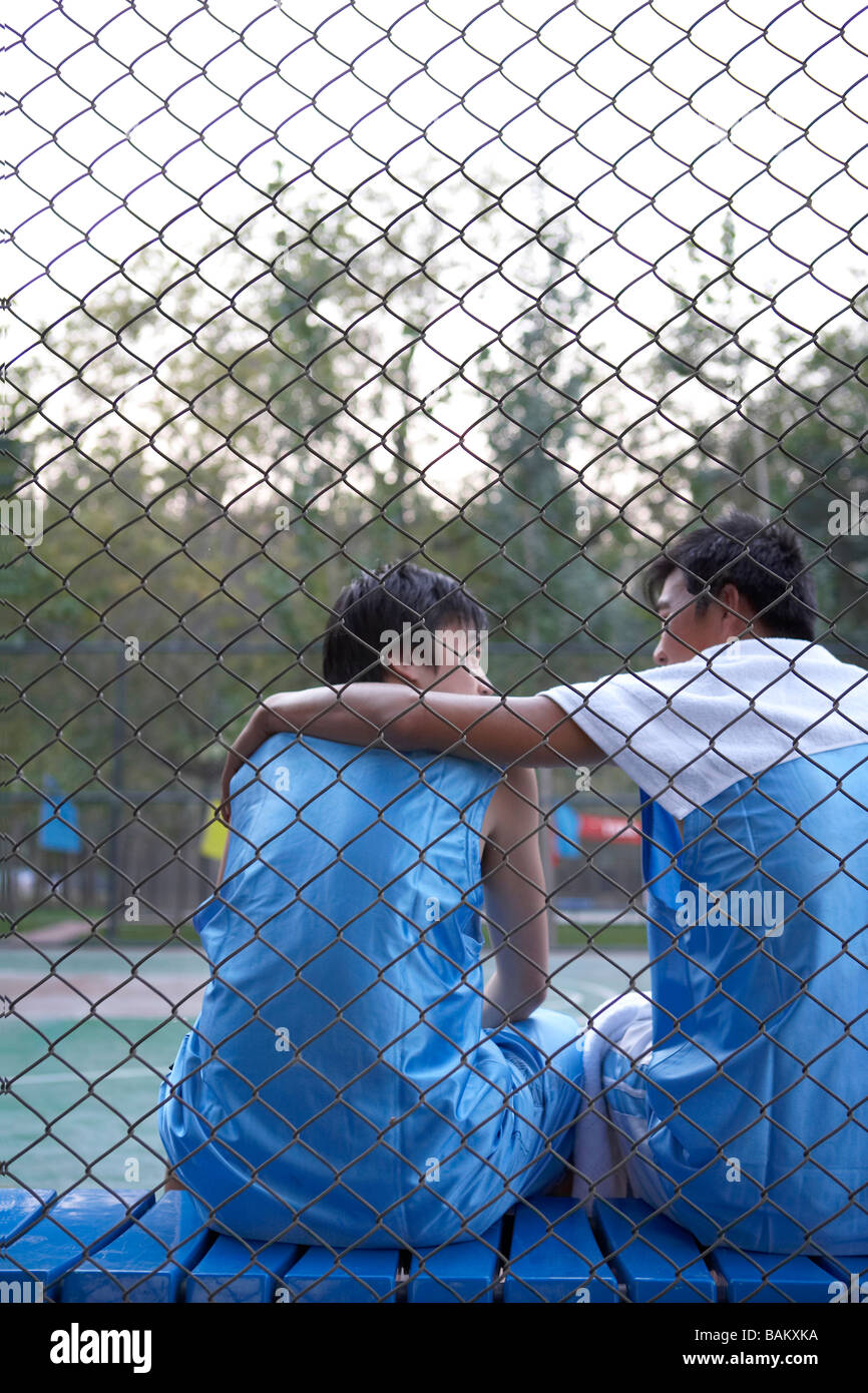 Junge Männer sitzen auf einer Bank neben einem Basketballplatz Stockfoto