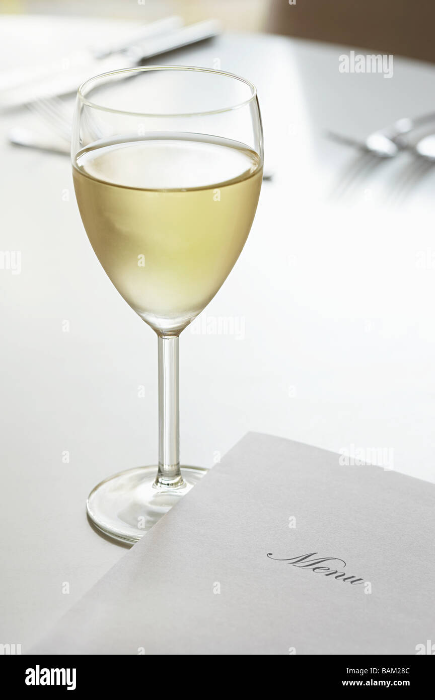 Glas Weißwein und ein Menü auf dem Tisch Stockfoto