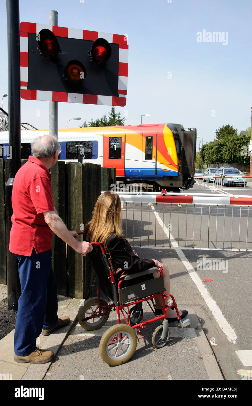 Weibliche ungültig Rollstuhlfahrer und männliche Betreuer warten an einem Bahnübergang England UK Stockfoto