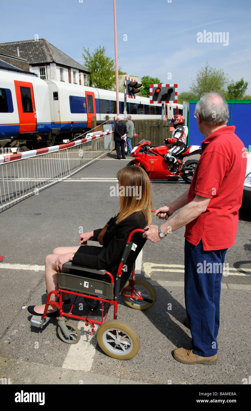 Weibliche ungültig Rollstuhlfahrer und männliche Betreuer warten an einem Bahnübergang England UK Stockfoto