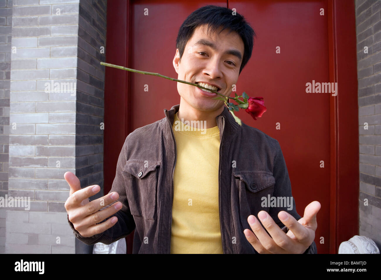 Junger Mann gestikulieren außen Haustür hält eine Rose im Mund Stockfoto