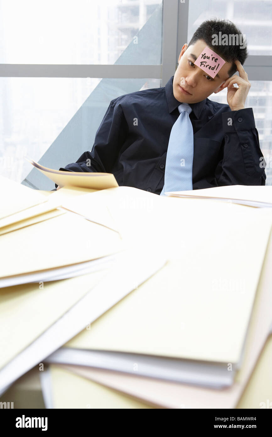 Geschäftsmann mit Notiz auf Stirn und Workpile Stockfoto