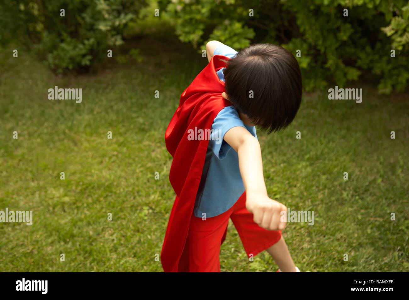 Junge In Red Cape spielen im Garten Stockfoto