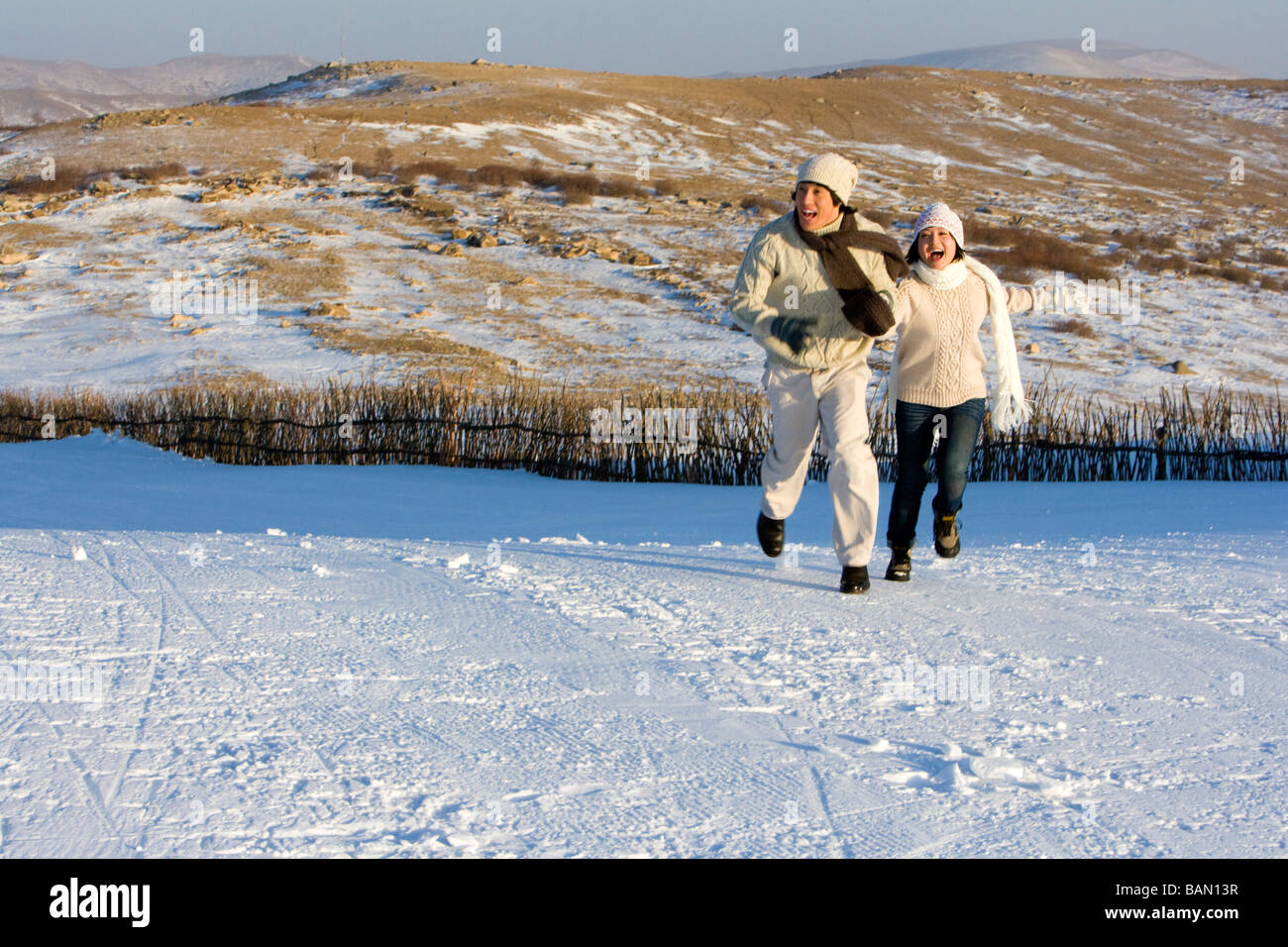 Junger Mann und junge Frau läuft im Schnee Stockfoto