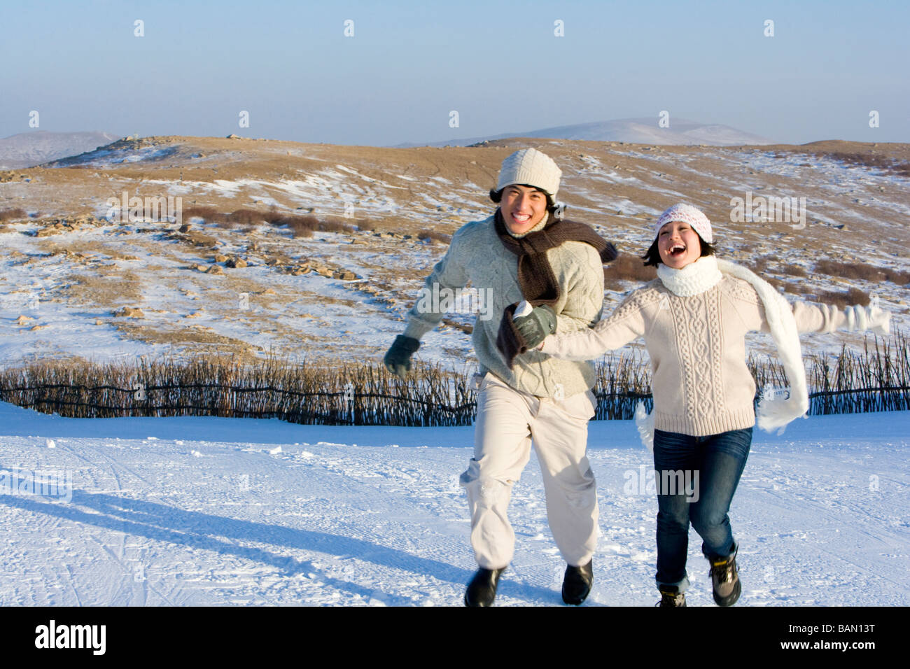 Junger Mann und junge Frau läuft im Schnee Stockfoto