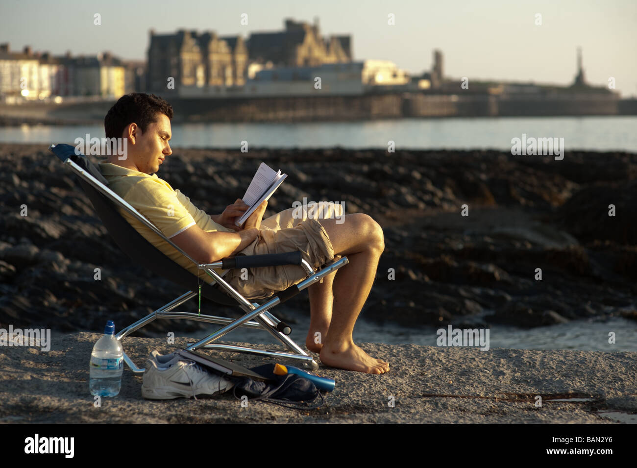 Junge männliche Studenten sitzen auf Stuhl am Strand von Aberystwyth, einem Text-Buch in der Sonne Wales UK Stockfoto