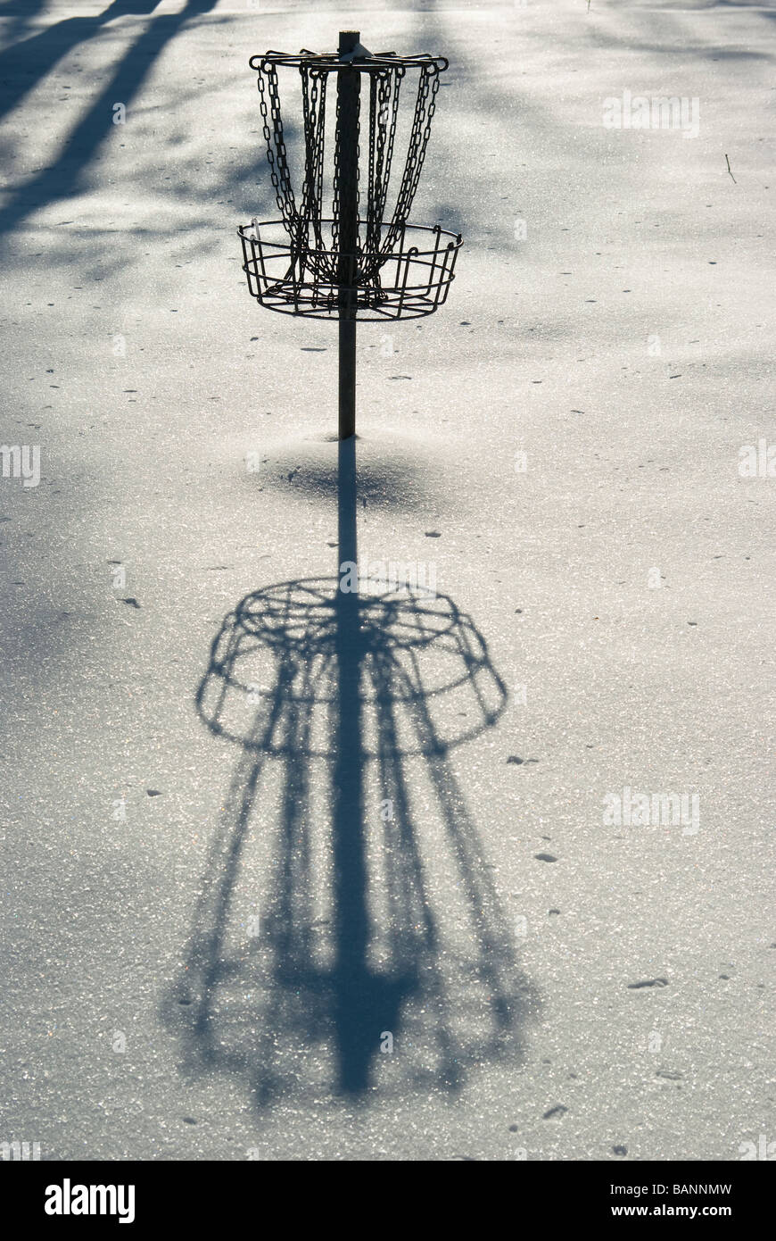 Ein Disc-Golf-Ziel wirft einen langen Schatten auf Neuschnee im Murdock Park in Lafayette, Indiana Stockfoto