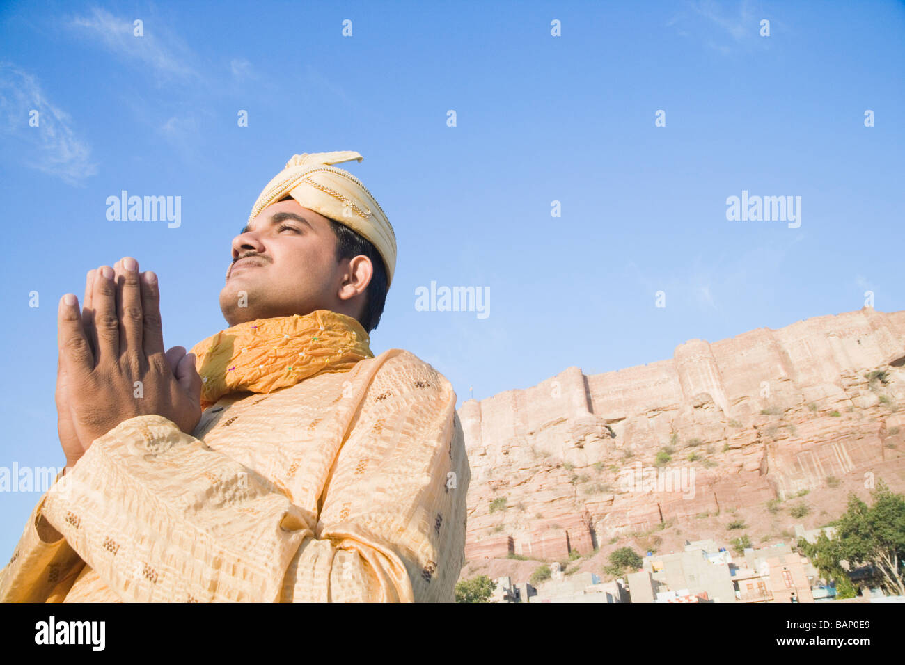 Niedrigen Winkel Blick auf einem Bräutigam im Gebet Position mit Festung im Hintergrund, Meherangarh Fort, Jodhpur, Rajasthan, Indien Stockfoto