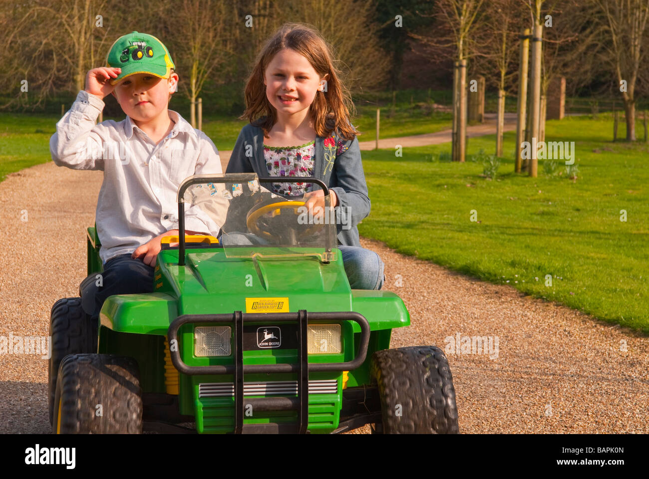 Ein Junge und ein Mädchen spielen auf eine batteriebetriebene Fahrt auf Spielzeug Jeep fahren auf eine private Fahrt auf dem Land Stockfoto