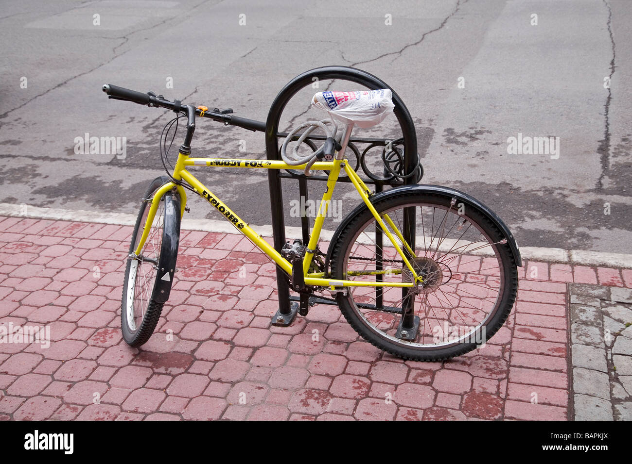 Ein Fahrrad gesperrt, um einen Fahrradträger mit einem Fahrradschloss der Sitz ist mit einer Plastiktüte zum Schutz vor dem regen bedeckt. Stockfoto