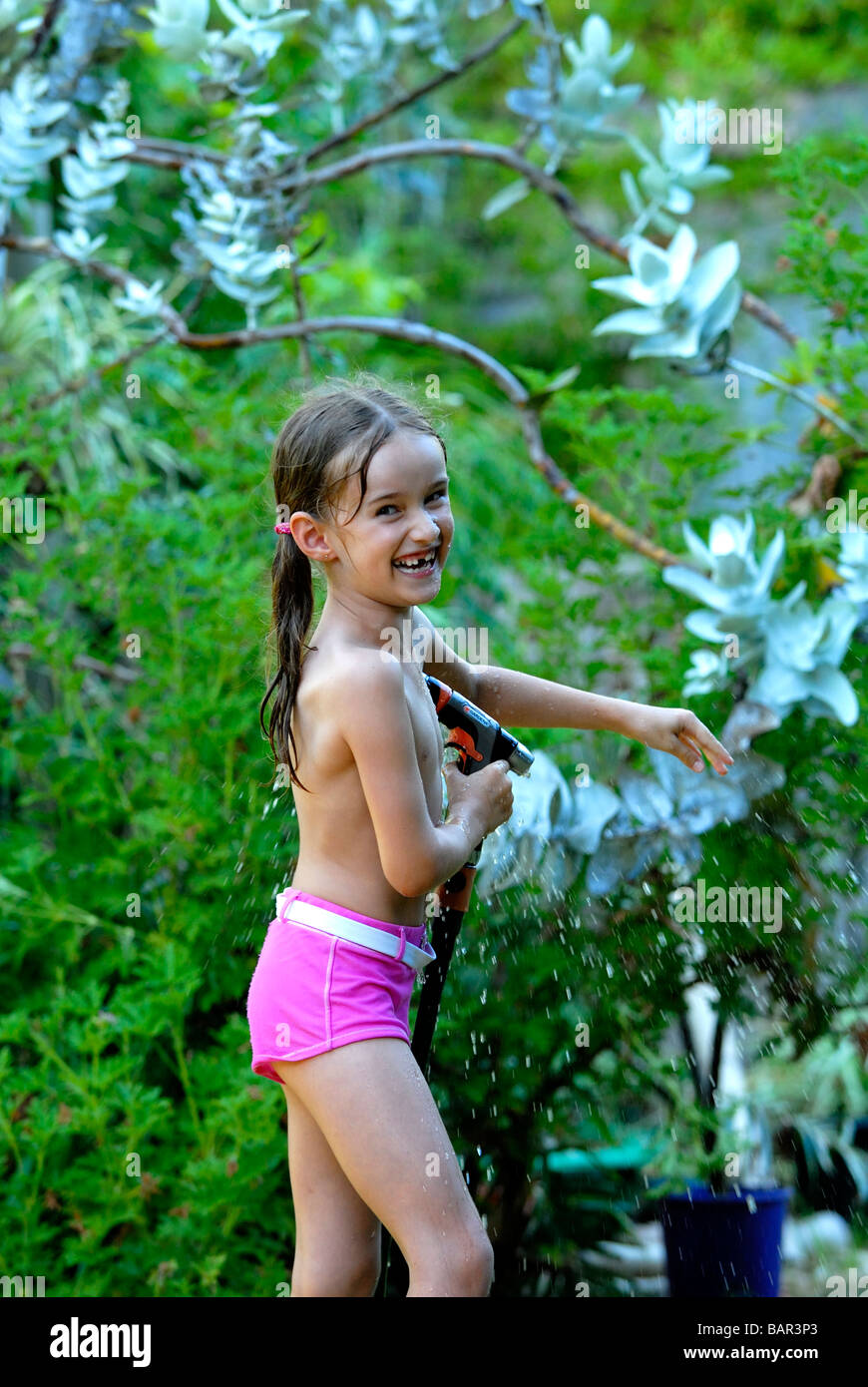 Sieben Jahre altes Mädchen spielen mit Schlauch im Garten Stockfoto