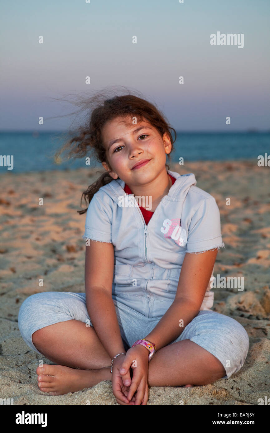 Hübsches kleines Mädchen sitzt am Strand bei Sonnenuntergang. Plage de Pampelonne, Ramatuelle, Var - Cote d ' Azur, Frankreich Stockfoto