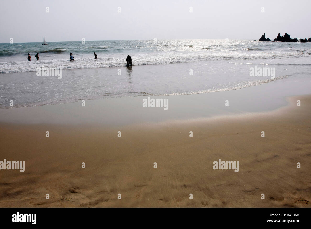 Menschen im Meer schwimmen und ein Segelschiff am Horizont in Arambol Beach im nördlichen Goa in Indien zu sehen. Stockfoto