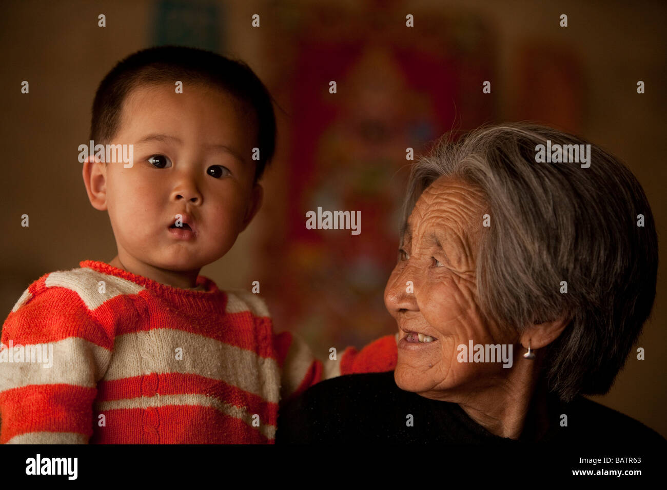 Changchun, Provinz Jilin, China.  Ein kleiner Junge in den Armen seiner Großmutter in ihrem kleinen Haus. Stockfoto