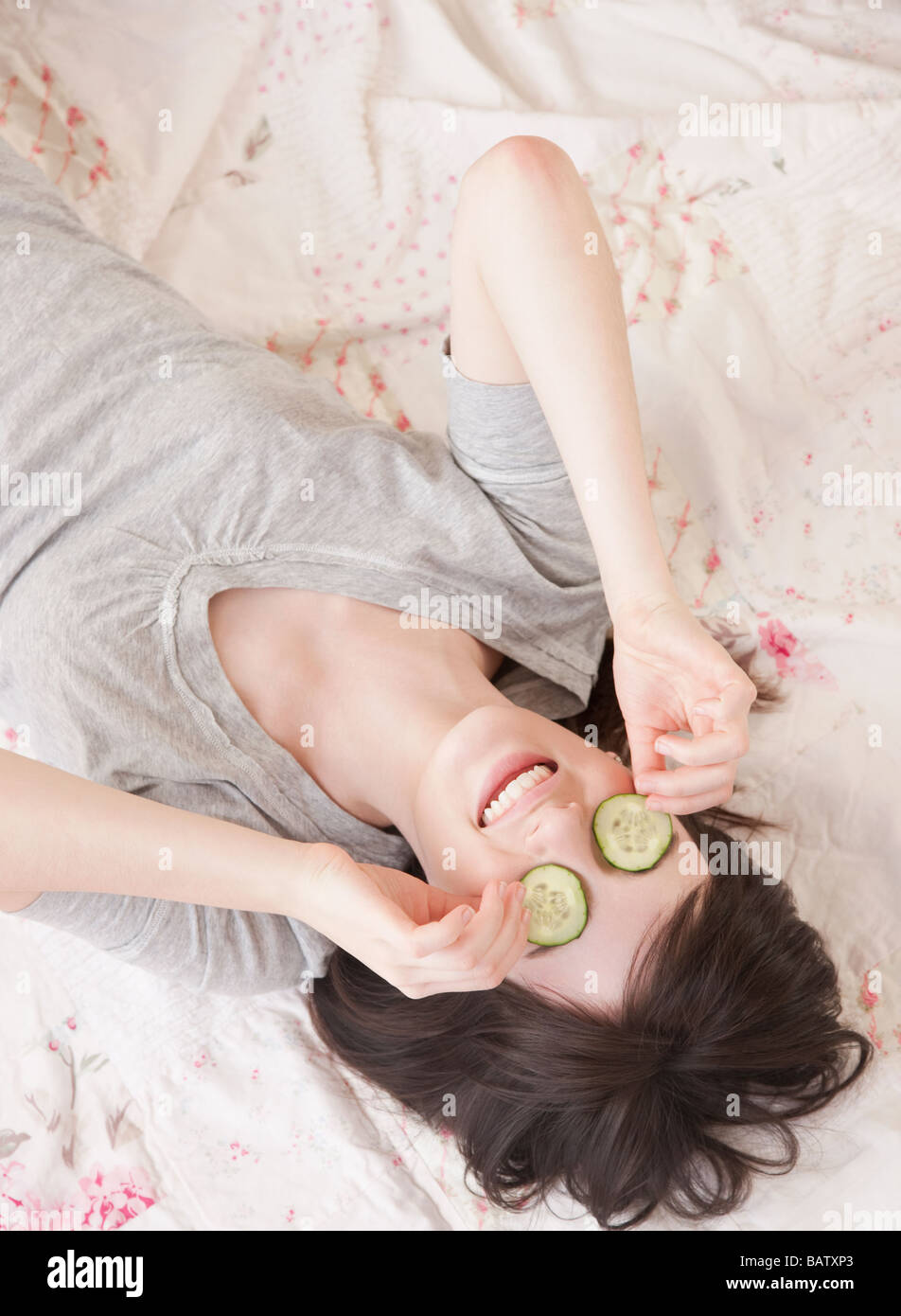 Junge Frau im Bett mit Gurken Gesichtsmaske Stockfoto