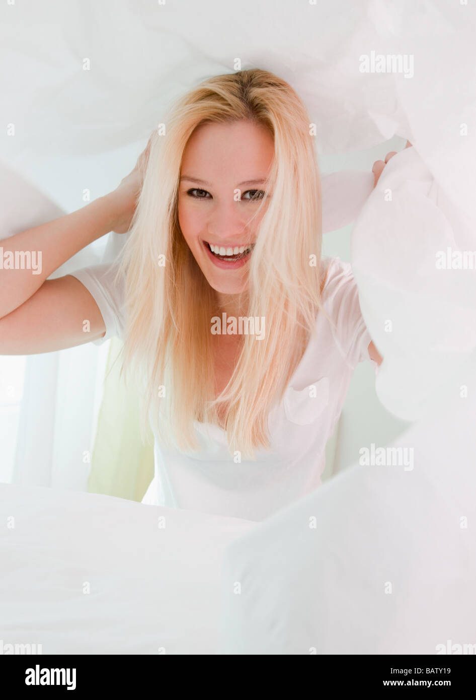 Porträt der jungen Frau Flickschusterei unter unberührten weißen Kissen Stockfoto