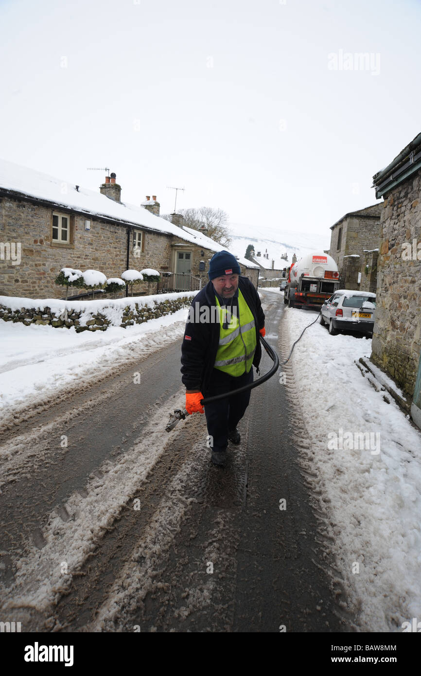 Eine Lieferung Mann liefert Gas an Haushalte durch dicken Schnee, Kettlewell Dorf, Yorkshire Dales. Stockfoto