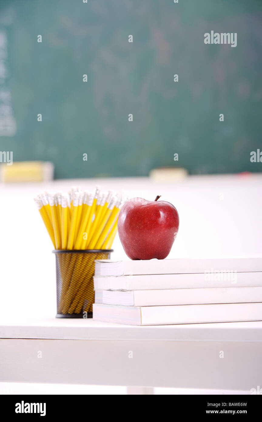 Apple-Lehrbücher und Bleistifte auf Schreibtisch vor Tafel Stockfoto